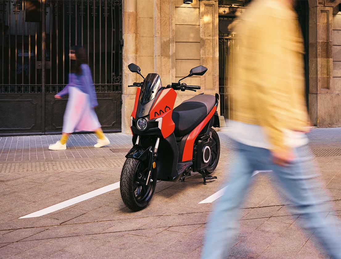 A couple walking around the parked SEAT MO 125 scooter