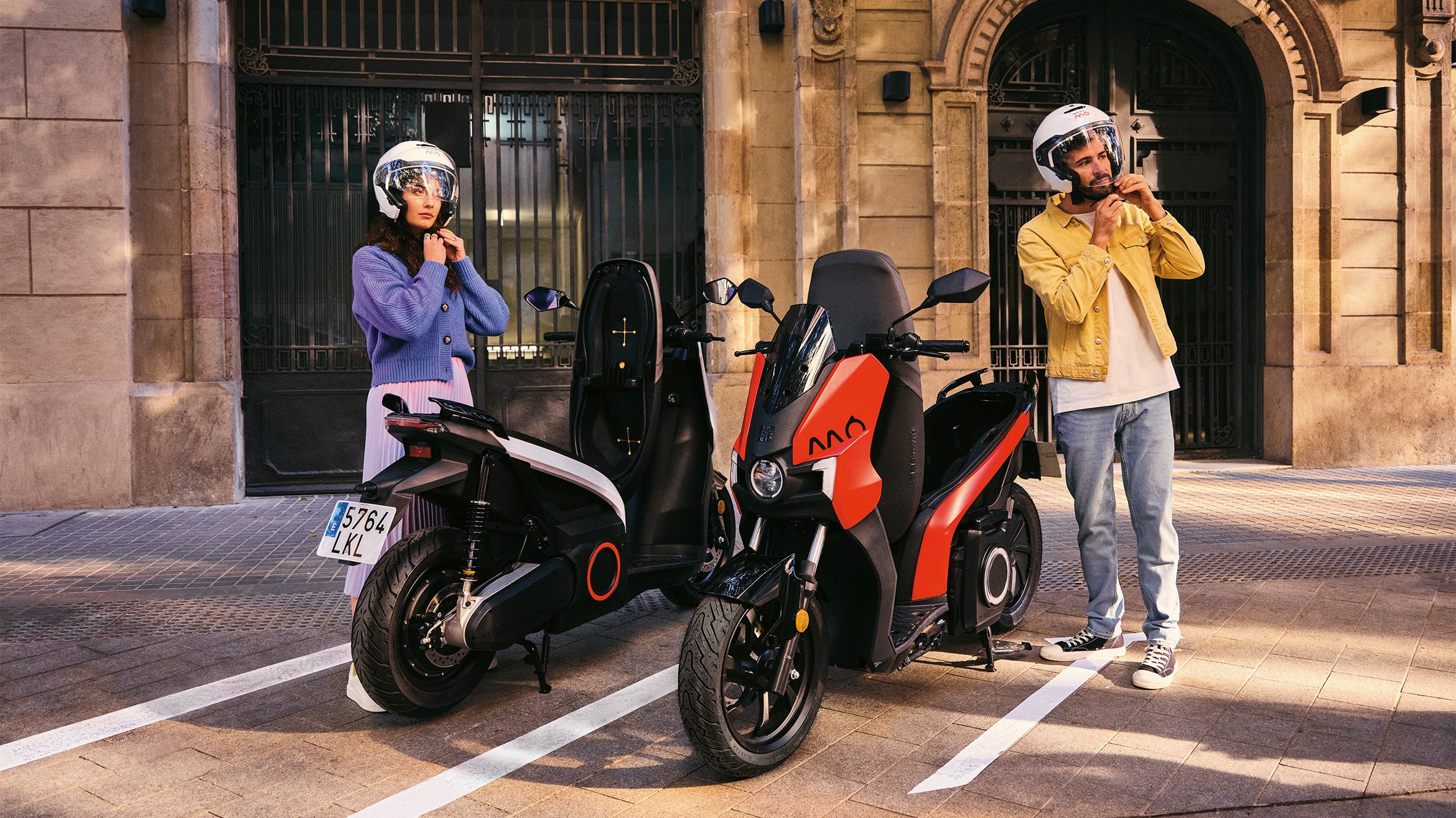 två personer personer som knäpper sina hjälmar bredvid SEAT MÓ 50 electric scooter